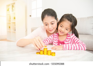 Happy Asian Mother Teach Her Daughter How To Saving And Calculate Money Everyday In The Living Room At Home. Family Activity Concept.