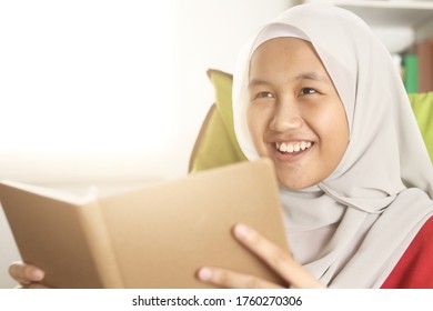 Happy Asian muslim girl wearing hijab smiling while reading book, leisure activity casual lifestyle, Islamic religion ethnicity