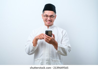 Happy asian muslim man holding and pointing on phone cellular over white background. Ramadan concept