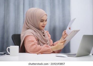 Happy Asian Muslim Woman Brown Hijab Working At Home With Laptop And Documents.