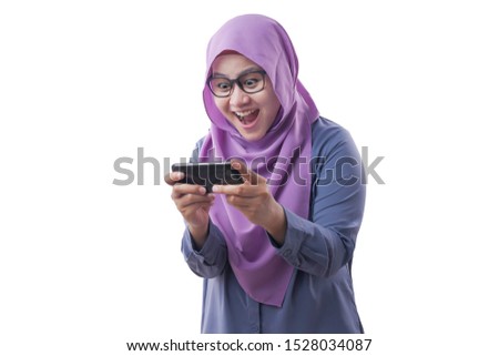 Happy Asian muslim woman excited to play games on her smart phone, isolated on white