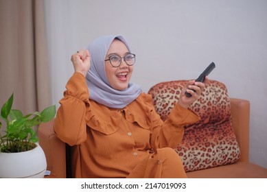 Happy Asian Muslim Woman Watching Tv At Home