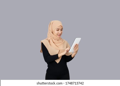Happy Asian Muslim Woman Wear Hijab Head Scarf Using Tablet Over Gray Background.