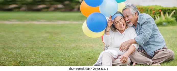 Happy Asian Old Couple Holding Balloons In The Front Lawn At Home. Senior Man And Elder Woman Spend Time Together In Backyard . Mature Husband And Wife Celebrating Anniversary In Garden. Copy Space
