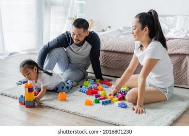 Happy Asian Parents Looking At Toddler Daughter Playing Building Blocks