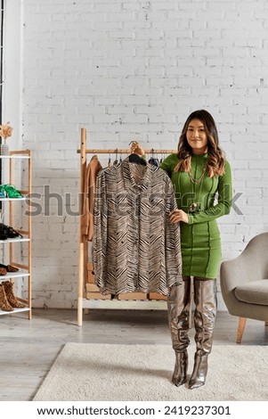 happy asian personal stylist showing trendy animal print blouse in private fashion atelier
