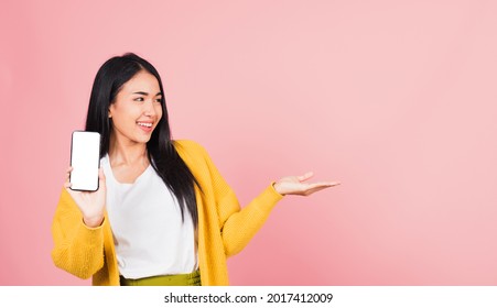 Happy Asian Portrait Beautiful Cute Young Woman Excited Holding Mobile Phone Blank Screen Presenting Product With Palm Of Hand At Empty, Studio Shot Isolated On Pink Background, Female Look To Space