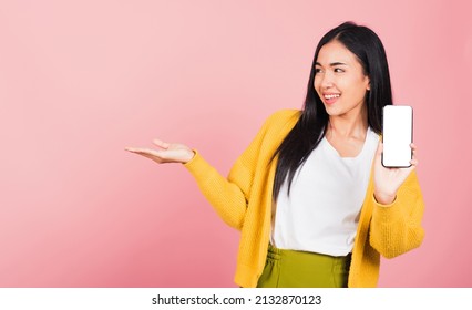 Happy Asian Portrait Beautiful Cute Young Woman Excited Holding Mobile Phone Blank Screen Presenting Product With Palm Of Hand At Empty, Studio Shot Isolated On Pink Background, Female Look To Space