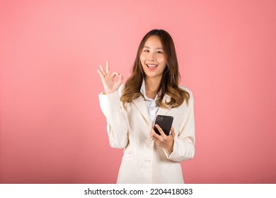 Happy Asian Portrait Beautiful Cute Young Woman Excited Holding Mobile Phone And Gesturing Ok Sign For Agree, Studio Shot Isolated On Pink Background, Thai Female Making Finger Symbol On Smartphone