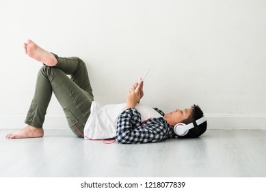Happy Asian school preteen boy using tablet and headphone, laying down on the floor.