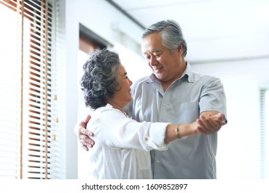 Happy Asian Senior Couple Dancing And Smiling At Home. Celebrating Wedding Anniversary.