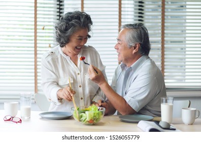 Happy Asian Senior Couple Doing Salad In Kitchen At House Together. Smiling Japanese Elderly Man And Woman Eating Healthy Food On Morning. Romantic Lover, Retirement Of Grandfather And Grandmother