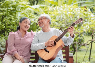 Happy Asian Senior Couple Elderly Man Playing Guitar Music Song Enjoy Having Fun Happiness Outside House Near Backyard Garden. Retirement Insurance Concept