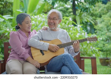 Happy Asian Senior Couple Elderly Man Playing Guitar While His Wife Singing Together Outdoors At Home, Activity Family Health Care, Enjoying Lifestyle During Retirement Life Having Fun Of Senior Older