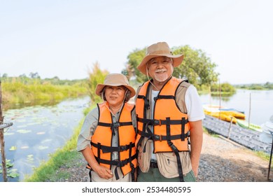 Happy Asian senior couple enjoy outdoor active lifestyle travel nature kayaking in the river on summer holiday vacation. Healthy elderly people in life jacket preparing to water sport canoe at lake. - Powered by Shutterstock