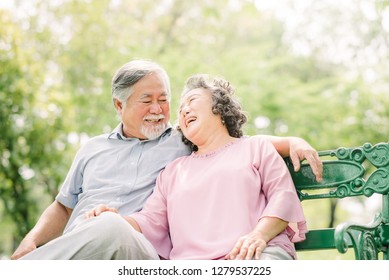 Happy Asian Senior Couple Laughing While Sitting On The Bench In The Park 