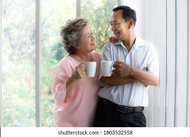 Happy Asian Senior Couple Looking Into Each Other Eyes Smiling While Enjoying Drink Morning Coffee At Home. Retired Older Grandfather Freedom On Finance. Good Retirement Plan Elder Person Lifestyle.