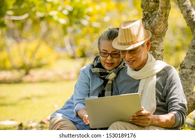 Happy  Asian Senior Couple Sitting At Park While Using Laptop Computer, Retirement Planning Family Lifestyle Healthy  Travel Vacation Concept