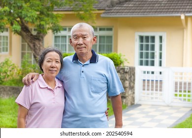 Happy Asian Senior Couple Standing In Front Of A House