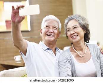 Happy Asian Senior Couple Taking A Selfie Using Mobile Phone.