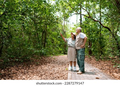 Happy Asian senior couple walking together on tropical forest trail. Retired elderly people man and woman enjoy and fun outdoor activity lifestyle travel nature hiking in jungle on summer vacation. - Powered by Shutterstock