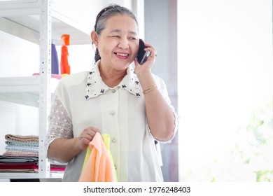 Happy Asian Senior Elderly Old Woman Housewife Using Mobile Phone While Doing Laundry At Laundry Room, Grandma Using Smartphone While Doing Housework And Cleaning Clothes At House.