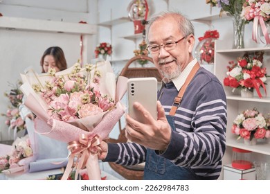 Happy Asian senior male florist owner selfie pictures and show floral bouquet arrangement with smartphone in valentine at bright flower shop, beautiful blossoms store, small business SME entrepreneur. - Powered by Shutterstock