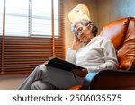 Happy Asian senior mature woman wearing glasses napping on sofa in living room after reading a book. Elderly retired grandmother enjoy indoor lifestyle with leisure activity and hobbies at home.