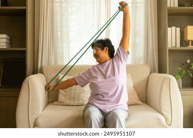 Happy Asian senior mature woman enjoy healthy lifestyle resistance band training exercise for stretching body muscle shoulder and arm on sofa in living room. Elderly self-care and home fitness concept - Powered by Shutterstock