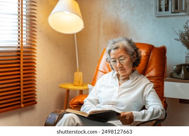 Happy Asian senior mature woman wearing glasses relaxing on sofa in living room and reading a book. Elderly retired grandmother enjoy indoor lifestyle with leisure activity and hobbies at home.
 - Powered by Shutterstock