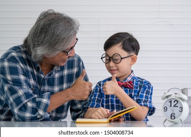 Happy asian senior retired grandfather teaching his grandson little boy do homework read and write at home. Grandpa praise grandson and do thumb up. Family relationship and people education concept.