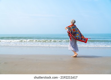 Happy Asian senior woman in blue dress walking on tropical island beach at summer sunset. Elderly retired woman relax and enjoy outdoor lifestyle activity in summer beach holiday travel vacation. - Powered by Shutterstock