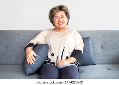 A happy asian senior woman sit on couch at home with smile and have make up on face. Concept of beautiful elderly woman, smiling and anti-aging.