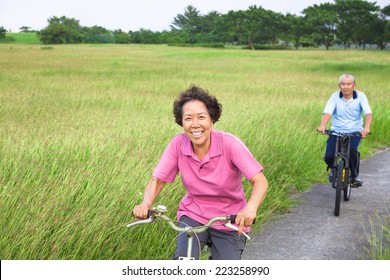 Happy asian seniors couple biking in the park.retirement and healthy lifestyle concept