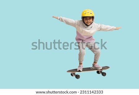 Happy asian smiling little girl playing skateboard wearing a helmet, Full body portrait isolated on pastel plain light blue background