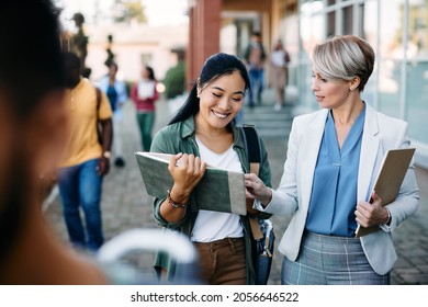 Happy Asian student communicating with her professor in front of university building. - Shutterstock ID 2056646522