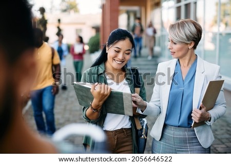Happy Asian student communicating with her professor in front of university building.