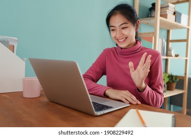 Happy Asian Student Waving In Greeting Online Tutor On A Laptop Computer At Home. Asia Woman Wear Long Sleeves Pink, Concept Of Online Learning At Home