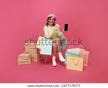 Happy Asian teen woman sitting on sofa holding shopping bags and smartphone isolated on pink background, Shopper or shopaholic concept. Сток-фото © 