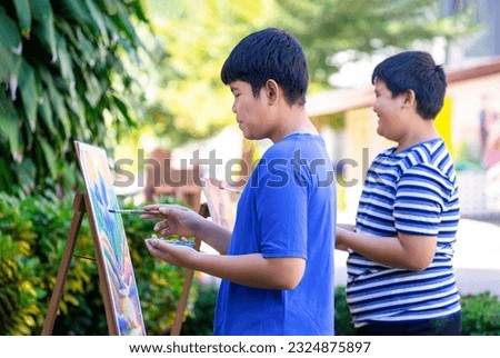 happy asian teenage boys painting on canvas,talking,laughter joyfully at outdoors school art club,teens activities,hobby,talent,drawing makes teens express their feelings and spark their creativity