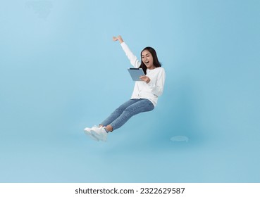 Happy asian teenage girl using tablet social media online floating in mid-air isolated on blue background. freedom fast internet technology concept. - Shutterstock ID 2322629587