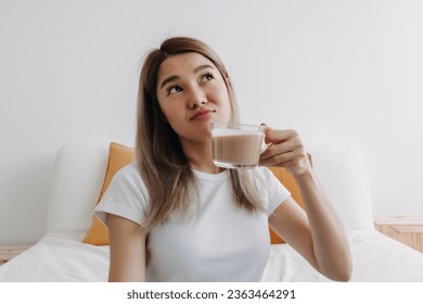 Happy Asian Thai woman holding coffee milk thinking something.
