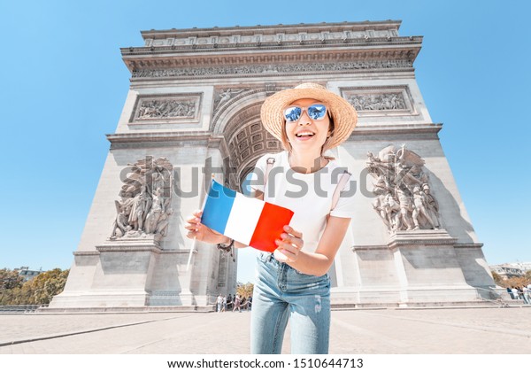 Happy Asian tourist girl enjoys the view of the\
majestic and famous Arc de Triomphe or Triumphal arch. Solo Travel\
and voyage to Paris and\
France