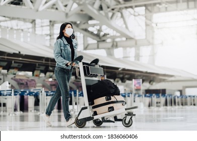 Happy Asian Tourist Woman With Mask Protection For Coronavirus Walking With Luggage Trolley Ready For Travel