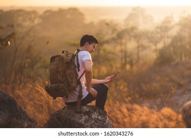 Happy Asian Traveler Man Is Enjoying With Beautiful Nature, Sunset During Using Smartphone. Technology, Wireless Communication.