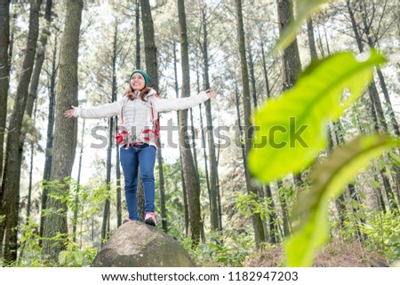 Happy asian traveler woman standing with raised arms on the forest