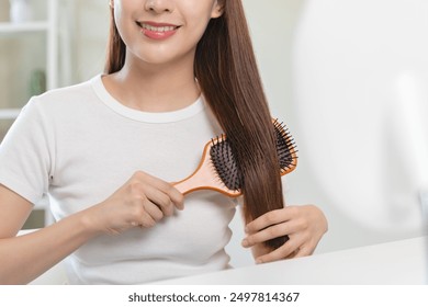 Mujer asiática feliz que cepilla el pelo por el peine de madera en la mañana.