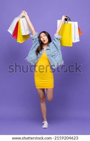Happy Asian woman carrying colorful shopping bags in purple color studio background