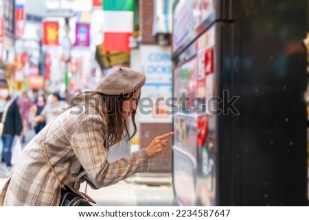 Happy Asian woman choosing and buying drinks on snack and beverage vending machine while shopping at shibuya, Tokyo, Japan. Attractive girl enjoy and fun outdoor travel city street on autumn vacation.