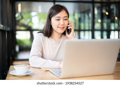 Happy Asian Woman Concentrated Working In The Coffee Shop By Using Laptop Computer. Confident Asian Girl Use Notebook Computer For Browsing The Internet And Social Network With Beautiful Smile.